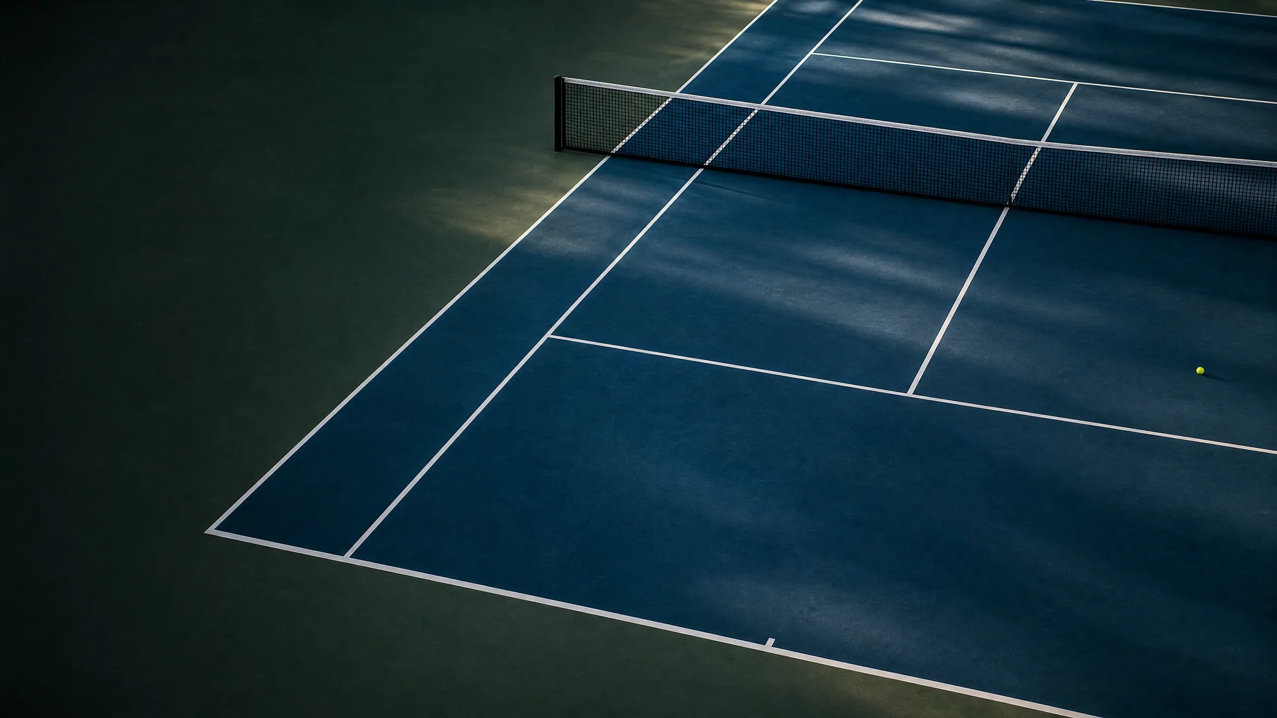 An empty blue hard tennis court with a ball near the service line